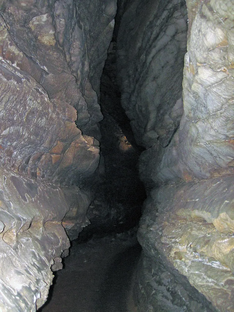 Narrow real limestone passage with a dark central trough, illustrating the confined shape described in Level 8 lore